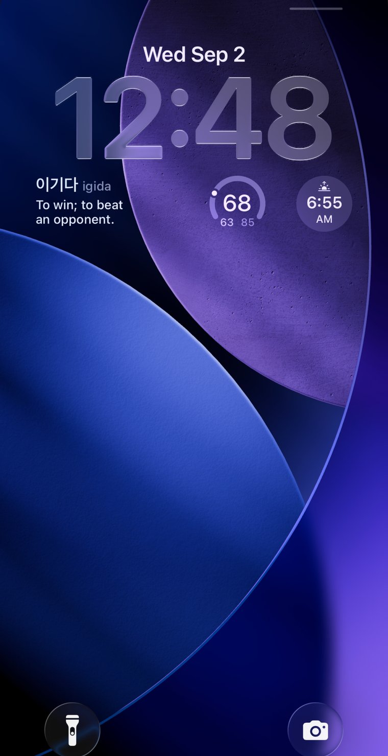 An iPhone lock screen with the Onymera widget showing the Korean word igida — to win; to beat an opponent.